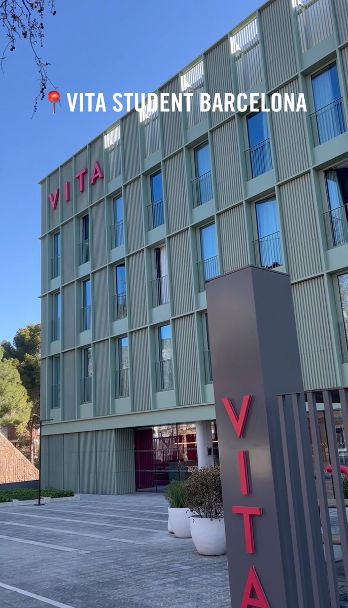 The image shows a modern multi-story building labeled "Vita" with vertical green panels. It appears to be a student accommodation place, "Vita Student Barcelona," as indicated by text on the image. The sky is clear and blue.