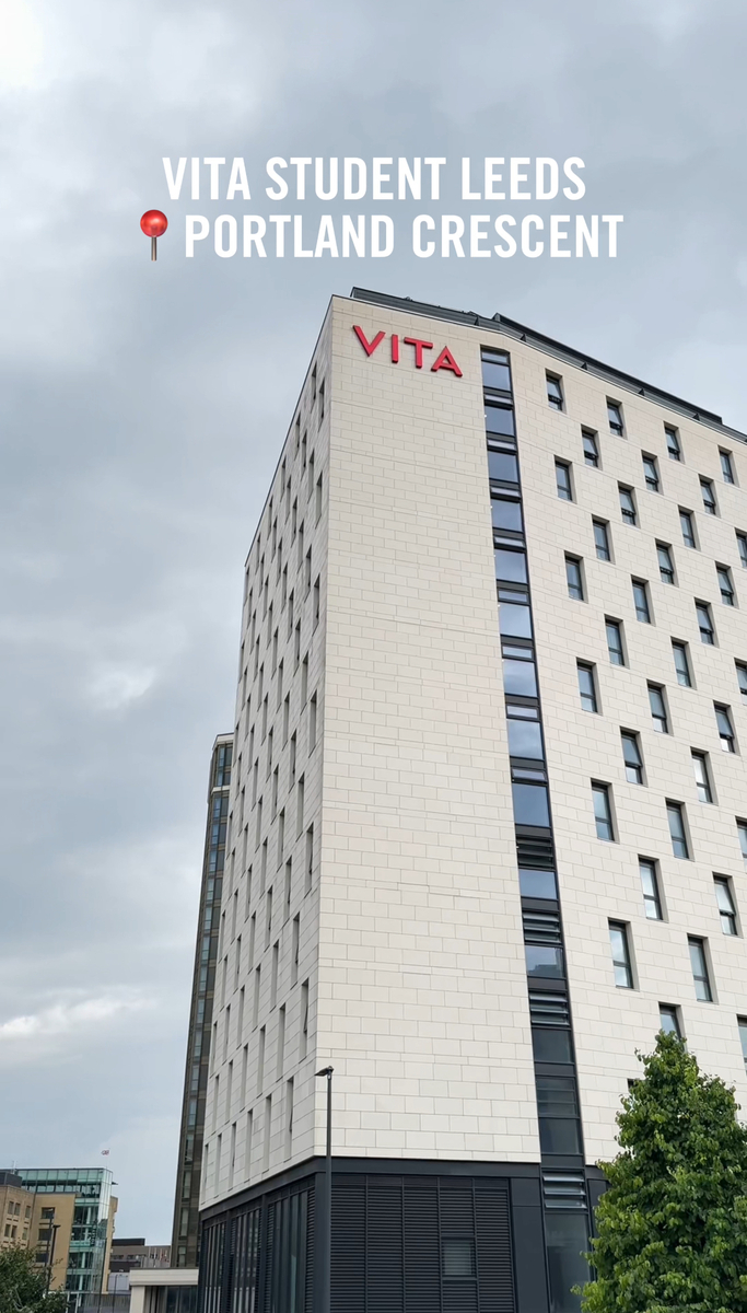 Tall modern building with "VITA" in red letters near the top looms over Portland Crescent. Overcast sky forms the backdrop, while text above reads "VITA STUDENT LEEDS 📍PORTLAND CRESCENT." A tree peeks into view at the bottom right, adding a touch of nature to the urban scene.