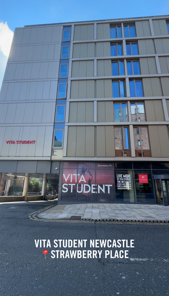 Street view of the modern multi-story building with the "Vita Student" sign. The facade features glass windows and beige panels at Strawberry Place. A promotional banner and entrance are visible at ground level, introducing Vita Student Newcastle as a prime residence choice.