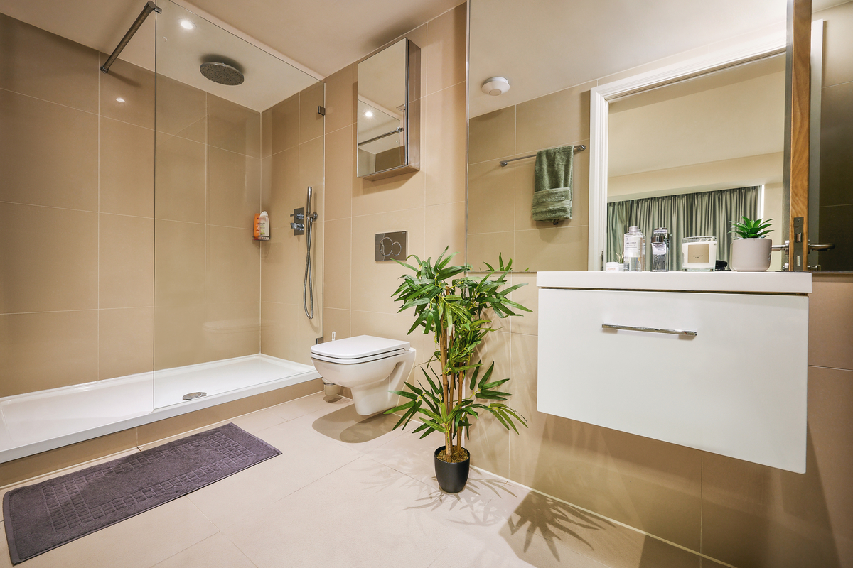 Modern Sheffield bathroom with beige tiles, a walk-in shower featuring a glass partition, wall-mounted toilet, and sleek white vanity with drawer. A potted plant adds greenery while a towel hangs by the mirrored cabinet above the sink.