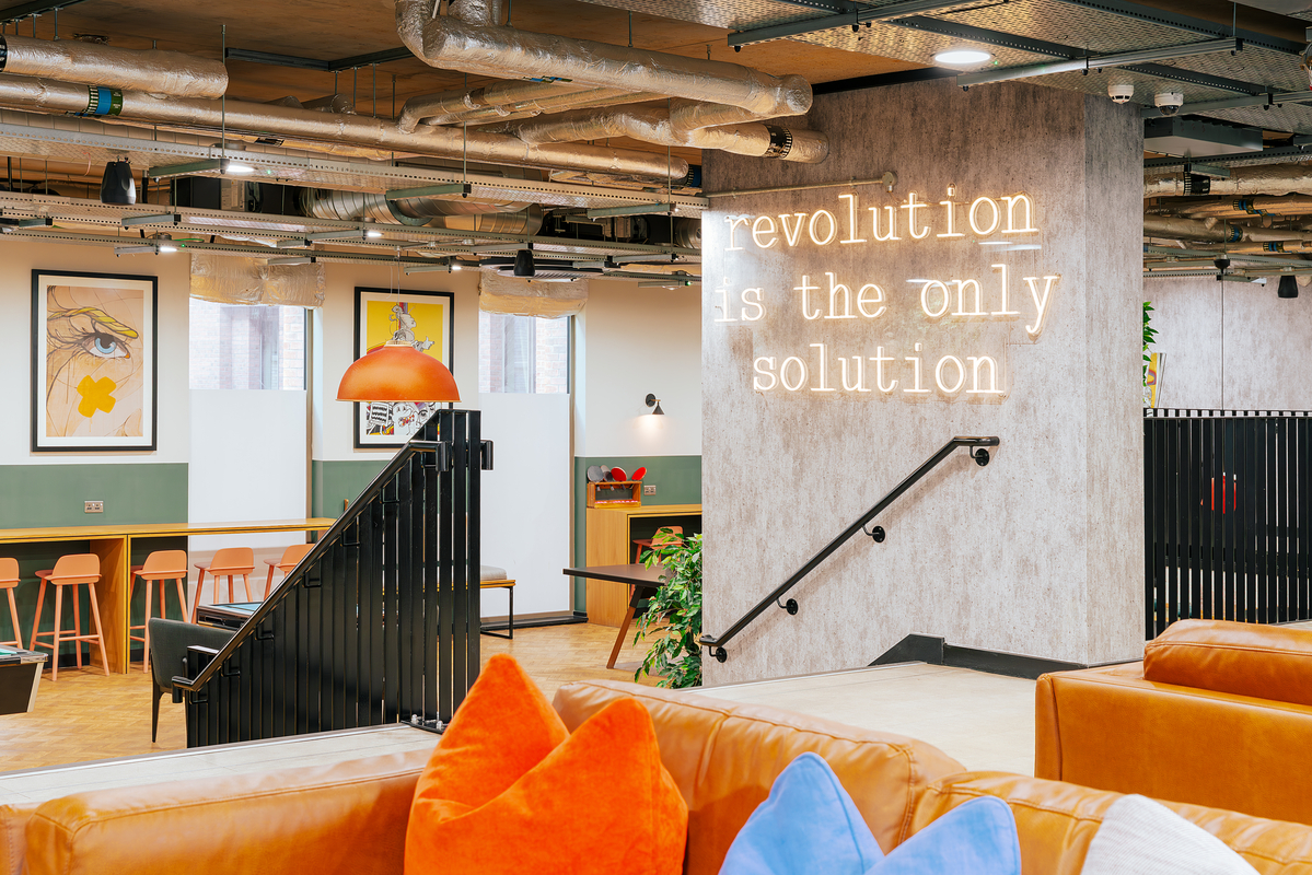 Chic, modern workspace with a neon sign reading "revolution is the only solution." The space features stylish seating, vibrant cushions, industrial decor, framed art, and a cozy lounge area.